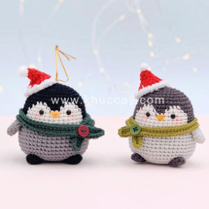 Deux pingouins crochetés en amigurumi gratuit, portant bonnet et écharpe de Père Noël, se tiennent côte à côte sur un fond clair aux lumières douces et floues. L'un porte une écharpe verte, l'autre une écharpe vert clair.