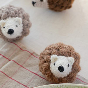 Deux petits hérissons en peluche, au visage blanc tricoté et au corps brun et moelleux, sont posés sur une surface en tissu. Parfait pour les fans d'animaux au crochet gratuits à télécharger, un autre jouet similaire est partiellement visible en arrière-plan.