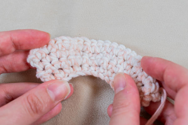 Deux mains tenant une courte bande courbe de crochet de couleur claire, mettant habilement en valeur les augmentations au crochet sur une surface beige.
