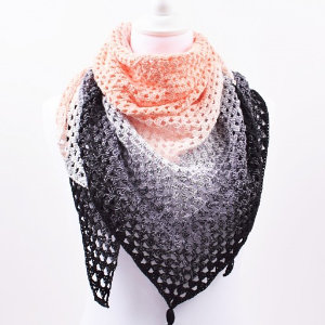 Une écharpe triangulaire crochetée, inspirée des châles au crochet, est présentée sur un mannequin blanc, présentant un motif de couleur dégradé qui passe du rose clair en haut au gris au milieu et au noir en bas.
