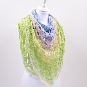 Un mannequin présente l'un de nos élégants châles au crochet, présentant un motif ouvert en dentelle et des couleurs dégradées qui passent du bleu clair au crème puis au vert pâle.