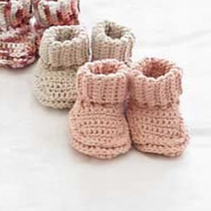 Deux paires de chaussons bébé au crochet, l'un beige et l'autre rose, sont présentées sur une surface blanche. Une troisième paire à rayures roses et blanches est partiellement visible en arrière-plan.