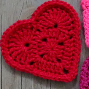 Un cœur rouge en crochet avec un motif texturé repose sur une surface en bois.