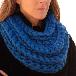 Une femme portant une grosse écharpe bleue tricotée à la main drapée autour de son cou sur un manteau noir, avec seulement la moitié inférieure de son visage visible.