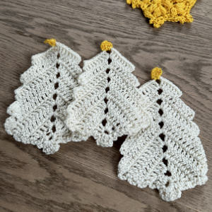 Trois décorations d'arbre de Noël blanches crochetées avec des sommets jaunes sont disposées côte à côte sur une surface en bois.