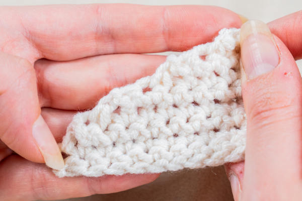 Gros plan de deux mains tenant un petit morceau de tissu blanc crocheté, montrant la texture et les points individuels créés avec les techniques de diminution au crochet.