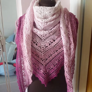 Un mannequin présente un châle tricoté triangulaire avec des motifs de dentelle complexes, passant du rose clair en haut au magenta foncé en bas.