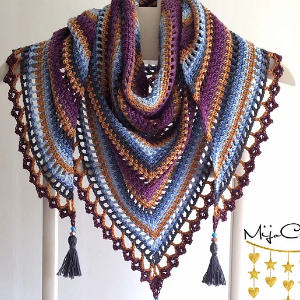 Un châle triangulaire coloré au crochet avec des rayures violettes, bleues, moutarde et marron, fini avec une bordure en dentelle et deux pompons - une inspiration parfaite pour ceux qui recherchent des grilles gratuites de châle au crochet.