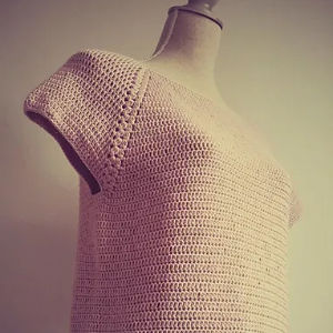 Un haut beige à manches courtes au crochet affiché sur une forme de robe sur un fond uni de couleur claire — parfait comme modèle top crochet gratuit à télécharger.
