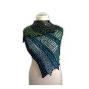 Un mannequin présente un châle tricoté avec un motif ajouré en dentelle dans des couleurs dégradées, passant du vert foncé au bleu profond avec des bords pointus - une inspiration parfaite si vous recherchez des modèles de crochet débutant gratuits.