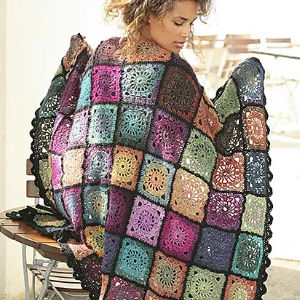 Une femme est assise sur un banc, drapée dans une couverture à carreaux colorée au crochet composée de carrés de grand-mère multicolores aux motifs complexes.