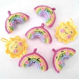 Porte-clés crochetés ornés d'arcs-en-ciel et de soleils disposés sur un fond blanc. Les arcs-en-ciel arborent des couleurs pastel bordées de rose, tandis que les soleils jaunes souriants arborent des joues roses.