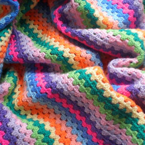 Une couverture bébé colorée au crochet avec des rayures en zigzag dans des tons de rose, violet, bleu, vert, jaune et orange, drapée de plis doux.