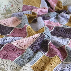 Une couverture bébé douillette au crochet, composée de carrés aux tons pastel de rose, violet, jaune et gris, est drapée doucement pour mettre en valeur son motif texturé et en dentelle.