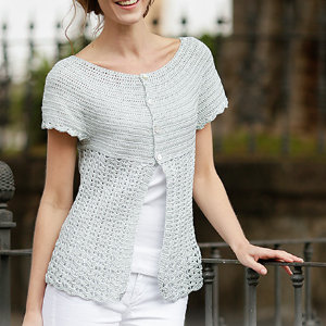 Femme portant un gilet gris clair à manches courtes au crochet pour femme avec un ourlet festonné et deux boutons sur le devant, associé à un pantalon blanc, debout à l'extérieur et souriant.