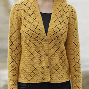 Une personne porte un cardigan tricoté jaune moutarde avec un motif ajouré en forme de losange, rappelant les gilets au crochet pour femme, boutonné sur le devant sur un haut noir.