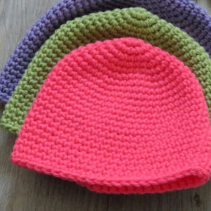 Trois chapeaux crochetés sont empilés sur une surface en bois. Présentés sous forme de modèles de crochet faciles et gratuits, le chapeau haut est rose vif, celui du milieu est vert et celui du bas est violet.