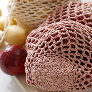 Gros plan d'un sac réutilisable rose au crochet, fabriqué à l'aide de modèles de crochet faciles et gratuits, rempli d'oignons et de pommes de terre, avec un autre sac en filet et des oignons et des pommes de terre en vrac en arrière-plan.