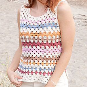 Une personne portant un haut au crochet sans manches à rayures horizontales crème, bleu, orange, marron, rose et bordeaux se tient à l'extérieur sur une surface sablonneuse - une inspiration parfaite pour les modèles gratuits de débardeurs au crochet.