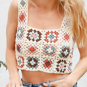 Une femme portant un haut court au crochet fait main avec un motif carré de grand-mère coloré dans des tons de crème, marron, rose, bleu et vert - une inspiration parfaite pour les modèles gratuits de débardeurs au crochet.