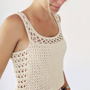 Une femme portant un haut sans manches de couleur crème au crochet avec un motif ouvert en dentelle sur les bretelles et les côtés, debout sur un fond blanc uni.