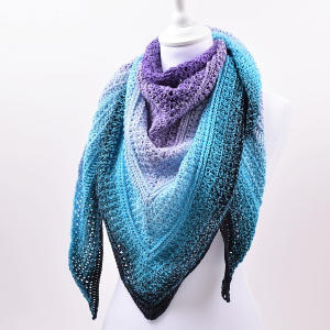 Un mannequin portant un châle triangulaire au crochet dans des tons dégradés de bleu, violet et noir, présenté sur un fond blanc uni.
