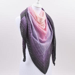 Un mannequin présente un châle triangulaire au crochet avec un dégradé ombré, passant du gris foncé sur les bords au lavande, au lilas et au rose clair vers le centre.