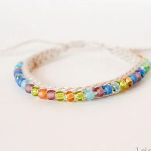 Un bracelet tressé blanc orné de petites perles rondes multicolores, notamment bleues, vertes, oranges et violettes, disposées sur deux rangées le long de la tresse.