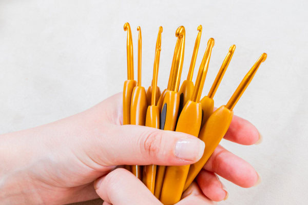 Une main tient un ensemble de crochets ergonomiques jaunes avec des poignées ergonomiques, disposés en éventail pour présenter différentes tailles sur un fond clair.
