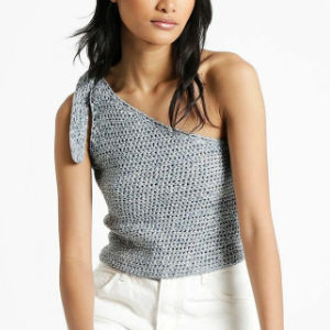 Une femme portant un haut gris crocheté à une épaule avec une cravate sur la bretelle et un pantalon blanc, debout sur un fond blanc uni.