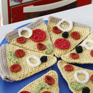 Une assiette bleue contient plusieurs parts de pizza crochetée, chacune garnie de morceaux de fil imitant du pepperoni, des olives, des oignons et des poivrons verts. Les tranches colorées, faites à la main, imitent une vraie pizza.