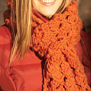 Une femme vêtue d'un manteau rouge et d'une épaisse écharpe orange au crochet sourit dehors. Seuls le bas de son visage et le haut de sa poitrine sont visibles.