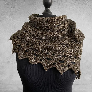 Un châle en crochet métallique foncé avec un bord festonné en dentelle est drapé autour d'un torse de mannequin noir sur un fond texturé gris.