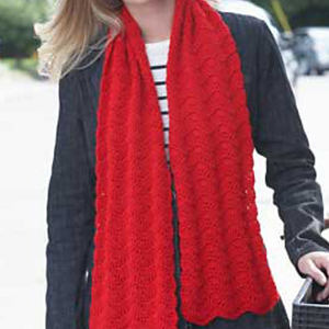 Une personne portant une veste noire et une écharpe rouge en tricot se tient dehors. L'écharpe présente un motif texturé ondulé, et la chemise rayée de la personne est partiellement visible sous la veste.