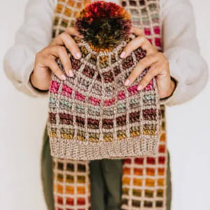Une personne porte un bonnet tricoté à rayures colorées et un pompon, ainsi qu'une écharpe multicolore assortie. Son visage est invisible.