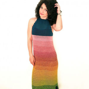Femme aux cheveux bouclés portant une robe au crochet sans manches à col licou avec un motif arc-en-ciel dégradé, debout sur un fond blanc uni.
