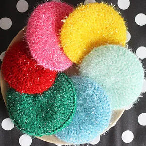 Une assiette contient six éponges rondes et colorées en rose, jaune, rouge, vert, bleu clair et bleu sarcelle, disposées sur une nappe noire à gros pois blancs.
