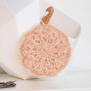 Une brosse à vaisselle ronde, de couleur pêche et texturée, avec un manche en bois, est posée contre un récipient blanc.