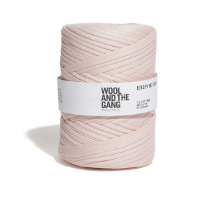 Une bobine de fil jersey rose pâle, ornée d'une étiquette blanche portant le nom de la marque Wool and the Gang. Le fil est soigneusement enroulé et sa texture est douce et plate.