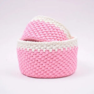 Un petit panier rond en osier tressé avec un corps rose et un bord blanc, sur un fond clair uni.