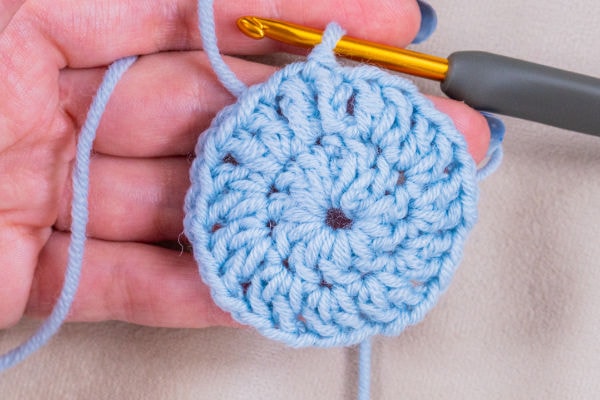 Une main tenant un cercle bleu clair au crochet avec un crochet doré inséré dans les mailles, parfait pour suivre un tuto granny au crochet.