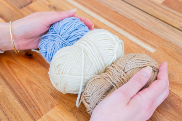 Deux mains qui tiennent trois pelotes de laine sur une table en bois