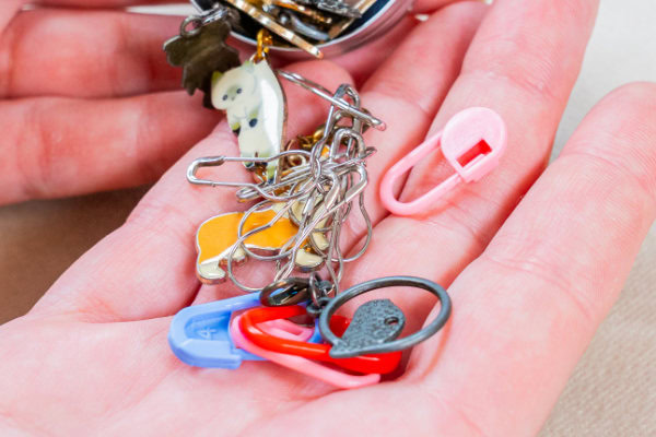 Gros plan d'une main tenant plusieurs marqueurs de points colorés en plastique et en métal emmêlés, ainsi que des porte-clés décoratifs - des outils parfaits pour tous ceux qui aiment crocheter en rond.