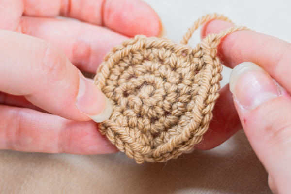 Gros plan sur des mains tenant une petite pièce ronde crochetée avec du fil beige, mettant en évidence les points complexes créés par une crocheteuse en spirale et montrant la texture détaillée.