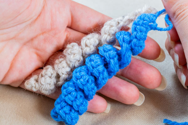 Gros plan d'une crocheteuse en spirale tenant deux spirales, l'une beige et l'autre bleue, avec un crochet travaillant activement sur le fil bleu.