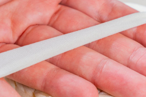 Gros plan d'une main tenant une bande de ruban de biais blanc, souvent utilisé en couture pour relier les bords ou en bricolage avec des matériaux comme le trapilho XL pas cher.