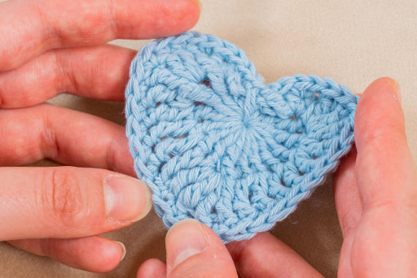 Une paire de mains tient délicatement un cœur crocheté bleu clair, illustrant l'art délicat de crocheter un cœur, sur un fond neutre.
