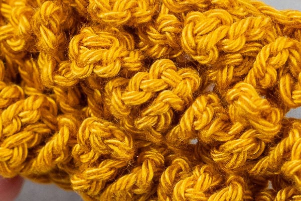 Gros plan sur un fil jaune crocheté au point d'astrakan pour créer un motif richement texturé et bosselé, avec des boucles et des torsades étroitement tissées créant une surface détaillée.