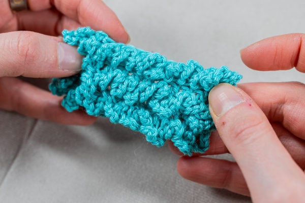 Personne qui tricote un morceau de fil en utilisant la technique du point d'astrakan au crochet.