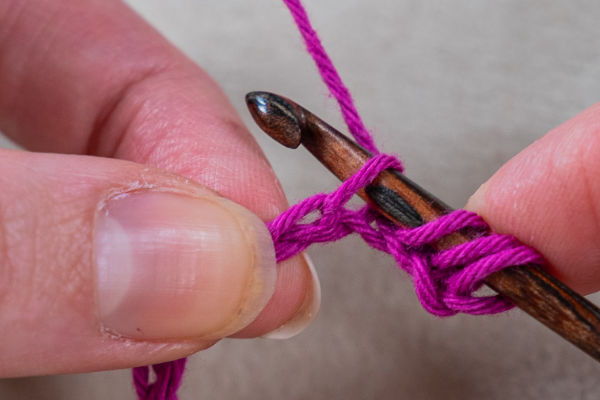 Gros plan de la main d'une personne tenant un crochet avec du fil violet, démontrant le processus d'un point de crochet tunisien.